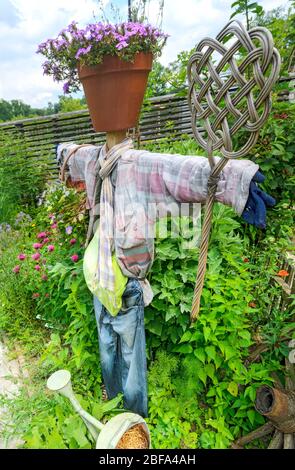 bird scarer with old clothes, a carpet beater and a head made from a flower pot in a rank growing garden