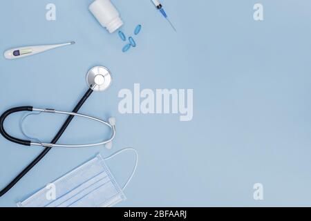 Flat lay of stethoscope, medical mask, termometr, pills and other medicine related items on blue background, Stock Photo