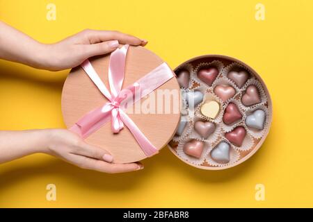 Female hands with delicious candies in box on color background Stock Photo