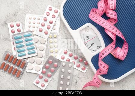 Weight loss pills, scales and measuring tape on grey background Stock Photo