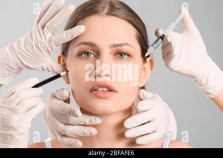 Young woman and hands of plastic surgeons with pencil and syringe on grey background Stock Photo