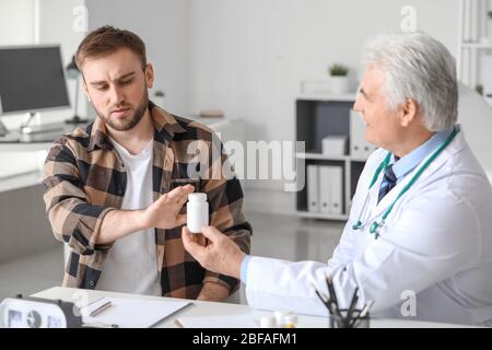 Young man refusing to take prescribed pills in clinic Stock Photo