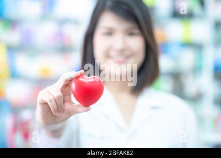 Asian women medical doctor holding a red heart ball with blurred background. Concept of health care. Stock Photo