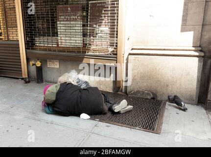 homeless person sleeping on a grate on w 57th street in Manhattan. Pigeons are seen wandering around the person, a symbol of income inequality Stock Photo