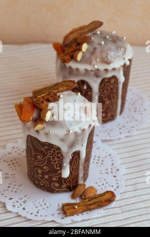 Vertical photo of two stylish traditional Orthodox Easter delicious cakes on the white napkins decorated by dried bananas, orange apricots, almonds an Stock Photo