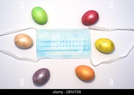 Many colored easter eggs laying around medical mask on the white background. Coronavirus Covid-19. Concept photo. Easter 2020. Stock Photo