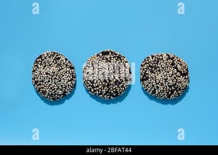 Three chocolate chip cookies with sesame seeds on top. Chocolate round cookies on a blue background. Tasty cookies background. Stock Photo