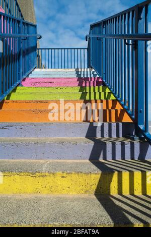 Concrete steps painted bright rainbow colours with a blue railing and a strong shadow pattern Stock Photo