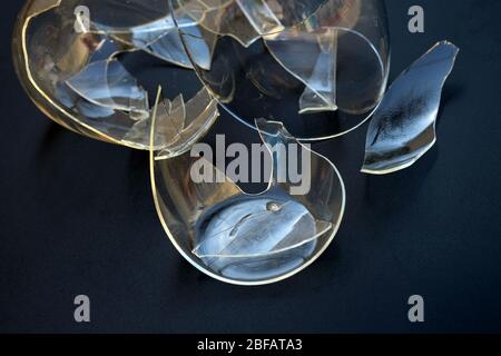 Broken cup on a black background. Mug with double bottom transparent shards. Shattered glass from the kitchen utensils. Danger of cutting shards. Stock Photo