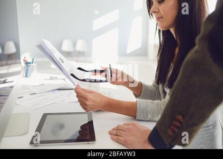 Crop businesswoman with coworkers working on laptop with papers Stock Photo