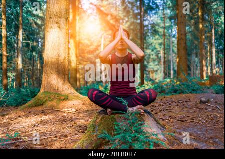 Woman meditating in woodland setting, morning yoga in the forest. Stock Photo