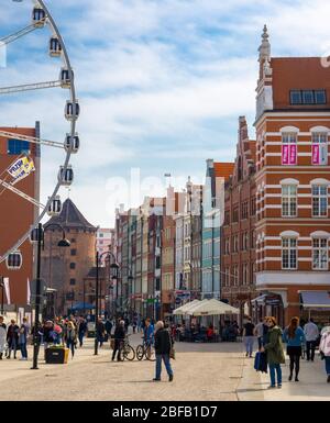 Gdansk, Poland, April 15, 2018: people walk along tourist pedestrian street near big ferris wheel, traditional typical orange buildings, tower gate Br Stock Photo