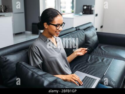 Cheerful young woman using a credit card and laptop computer to shop online from home Stock Photo