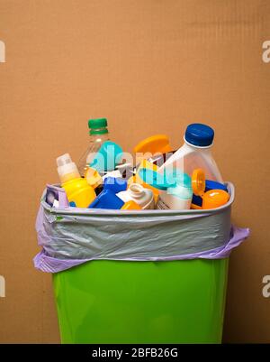 Colorfull plastic waste in the green trash can on brown bacground Stock Photo
