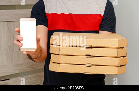 Man from delivery service holding pizza boxes and smartphone with mock up. Internet food order. Stock Photo