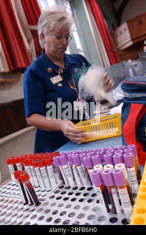 A NHS National Blood Service nurse packs blood donated at a collection centre into storage bag. In the foreground is a rack of blood samples in Vacuta Stock Photo