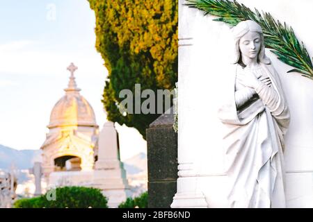 sculpture of a saint maria woman with crossed hands in an old cemetery.  stoned statue praying at cemetery. Graveyard old weathered stone sad mother s Stock Photo
