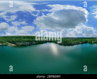 Colorful sky panorama with white clouds and a blue sky. Incredibly beautiful landscape. Granite overhangs of a quarry over water in the midst of green Stock Photo