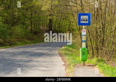 Bus stop with no smoking sign and green garbage bin beside road through forest, Brennbergi ut, Sopron, Hungary Stock Photo