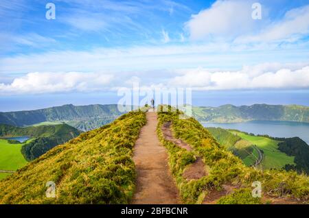 A path leading to viewpoint Miradouro da Boca do Inferno in Sao Miguel Island, Azores, Portugal. Amazing crater lakes surrounded by green fields and forests. Tourist at the end of the scenic way. Stock Photo