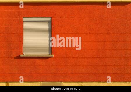 Facade with bright colors red orange yellow pedestal and a window shutter sideways horizontal line pattern Stock Photo