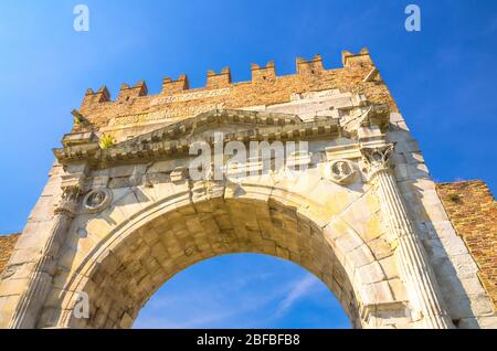 View from below of ancient brick wall and stone gate Arch of Augustus Arco di Augusto ruins in old historical touristic city centre Rimini with blue s Stock Photo