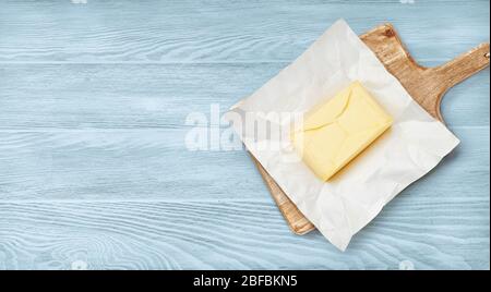 Piece of butter on package paper and wooden board. Top view of butter on blue wooden background. Stock Photo