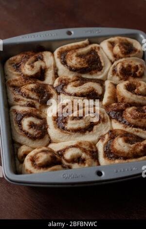 Unbaked cinnamon rools inside grey metal tin on dark wood background Stock Photo
