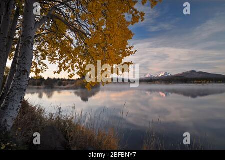 Autumn sunrise reveals snow capped Three Sisters and Broken Top peaks reflecting in this small pond at Central Oregon’s Black Butte Ranch. Stock Photo