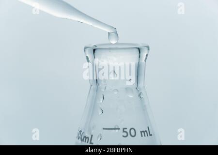 close up clean clear water drop in to glass flask in blue medical research science laboratory background