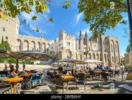 Tourists enjoy a meal at a sidewalk cafe in front of the medieval Pope's Palace in the Provence region of Avignon France as a tourist tram drives by Stock Photo