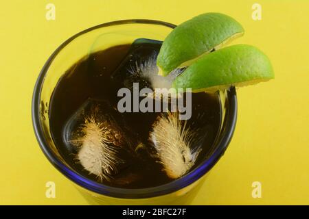 Close up of glass of iced black tea with ice cubes with lime wedges on yellow background Stock Photo