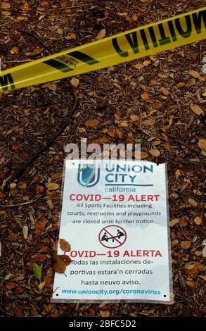 Covid-19 alert sign on ground at exercise area closed off with yellow caution tape  in Cann Park in Union City, due to covid-19 virus pandemic, California Stock Photo