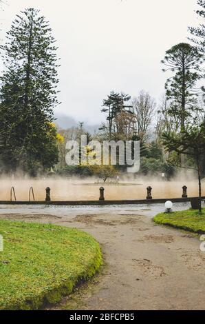 Furnas, Azores, Portugal - Jan 13, 2020: Hot spring iron water thermal pool in Terra Nostra Garden. The pool is surrounded by green botanical garden. Portuguese tourist attraction. Stock Photo