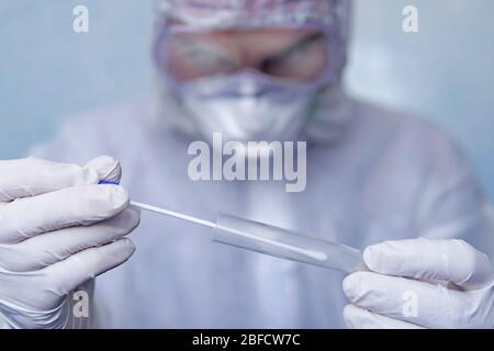 Hands in medical gloves holding empty plastic tube with blue cap for collection of analysis. a man in a chemical protection suit holds a test tube for Stock Photo