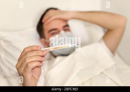 Sick man lying on bed checking his temperature at home in the living room. the inscription body temperature on the mercury thermometer Stock Photo