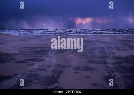 A cold windy evening by the sea with dark clouds and rain rolling in from the Riga bay with trails of sand blown by strong winds Stock Photo