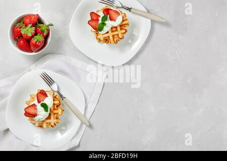 Beautiful breakfast. Belgian Viennese waffles decorated with cream and strawberries, tea and a checkered napkin on a light background. Top view. Stock Photo