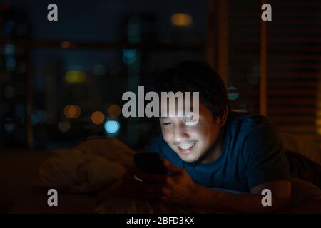 Closeup Asian man sleeping and using smart mobile phone for social network or video conference call and face time to her lovers on bed over blur city Stock Photo