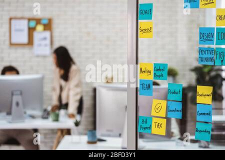 Various post it notes of business strategy wording over the glass wall in office or coworking space, business colleagues working and discussing togeth Stock Photo