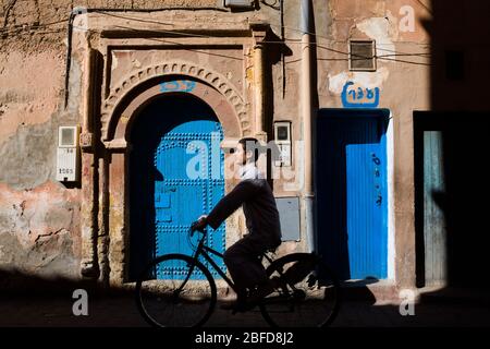 Local cyclist passing by an ornate turquoise door in the Western Sahara, Morocco. Stock Photo