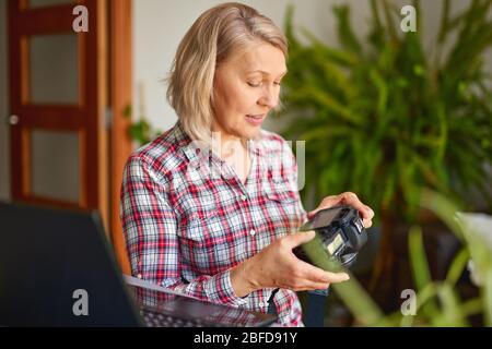 Portrait of attractive mature female photographer holding camera, looking at camera. Stock Photo
