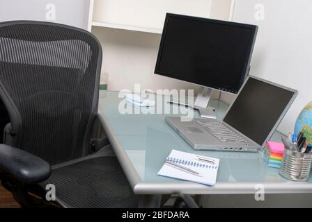 Empty view of deserted office cubicle featuring a desk chair, laptop computer and blank secondary screen for creative work Stock Photo