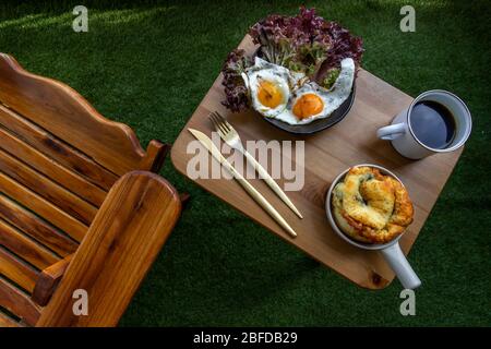 Breakfast with Spinach brioche, Two fried eggs, Oak Leaf lettuce served with Black coffee on wooden table at balcony. Selective focuse. Stock Photo