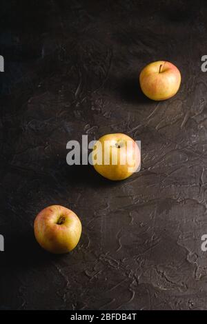 Fresh sweet three apples in row on dark black textured background, angle view Stock Photo
