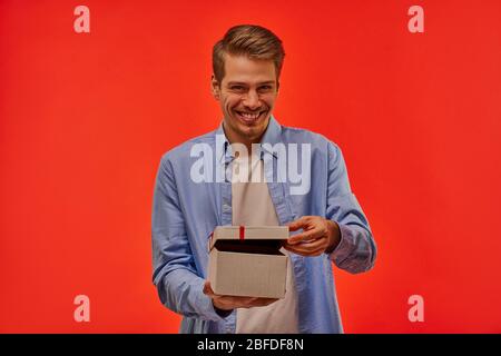 The fair-haired guy cunningly, cheerfully, fervently looks at the camera and opens the box to the viewer. Stock Photo