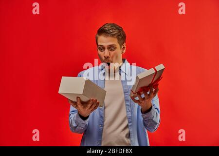 Surprised guy in a blue shirt looks in an open white box with a red ribbon. Stock Photo