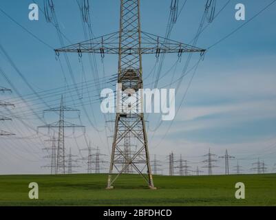 Pylons of high-voltage power lines in front of a blue sky with clouds on a green field, electrical industry. Stock Photo