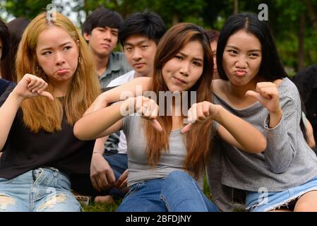 Stressed young group of friends giving thumbs down together at the park Stock Photo