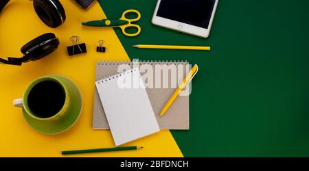 Stationery on the table top view. Yellow and green bright background. Notepad for notes with place for text. Work at home. A cup of coffee. Layout Stock Photo
